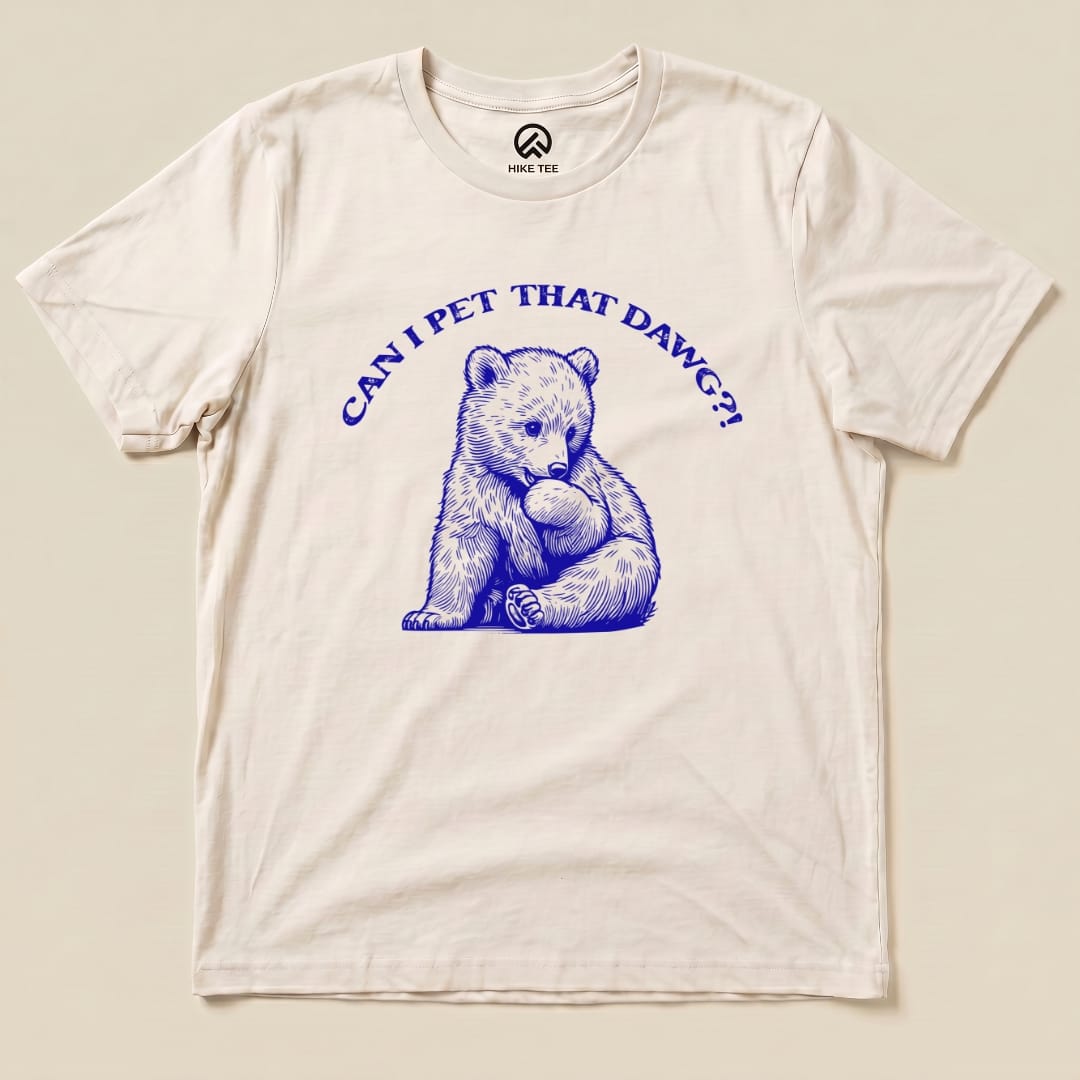 The "Pet That Dawg Shirt" features a blue graphic of a playful bear cub with the text "CAN I PET THAT DAWG?!" above it on a cream t-shirt.