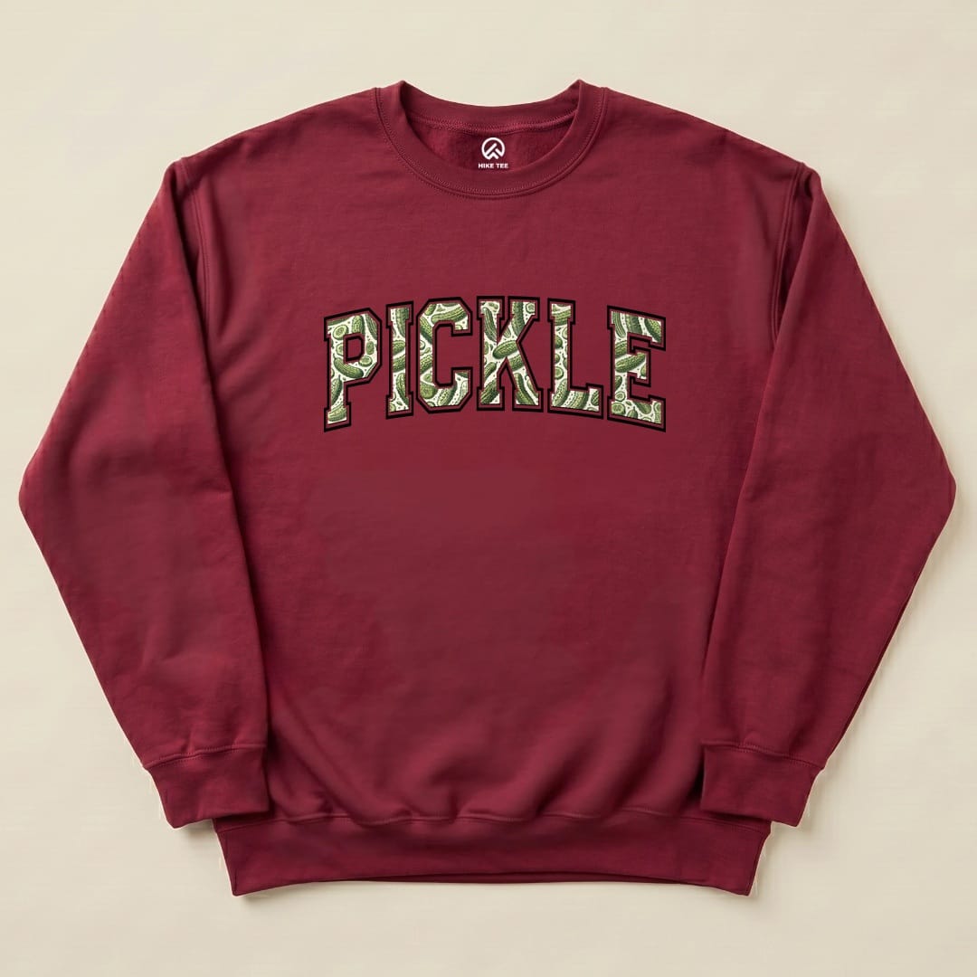 A maroon "Pickle Camping Sweatshirt" featuring large, bold text that reads "PICKLE" in a playful camo design.