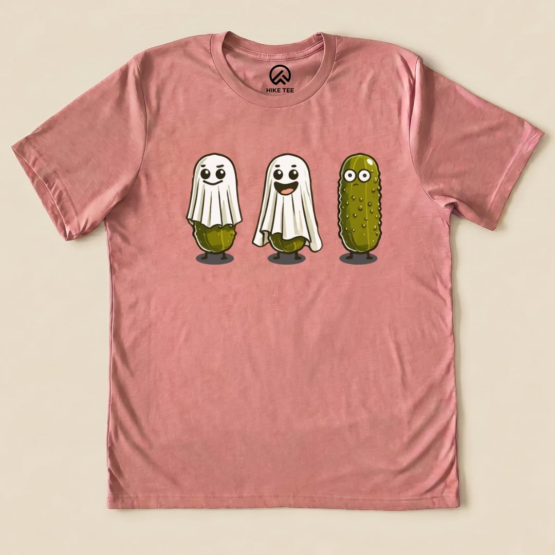 The Pickle Ghosts Shirt features three playful pickle characters, two dressed as ghosts and one smiling, on a pink graphic t-shirt.