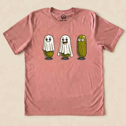The Pickle Ghosts Shirt features three playful pickle characters, two dressed as ghosts and one smiling, on a pink graphic t-shirt.