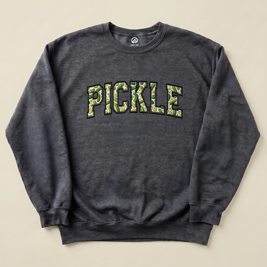 A dark grey graphic sweatshirt features the word "PICKLE" in a fun, green pickle-patterned design, showcasing a playful outdoor theme.