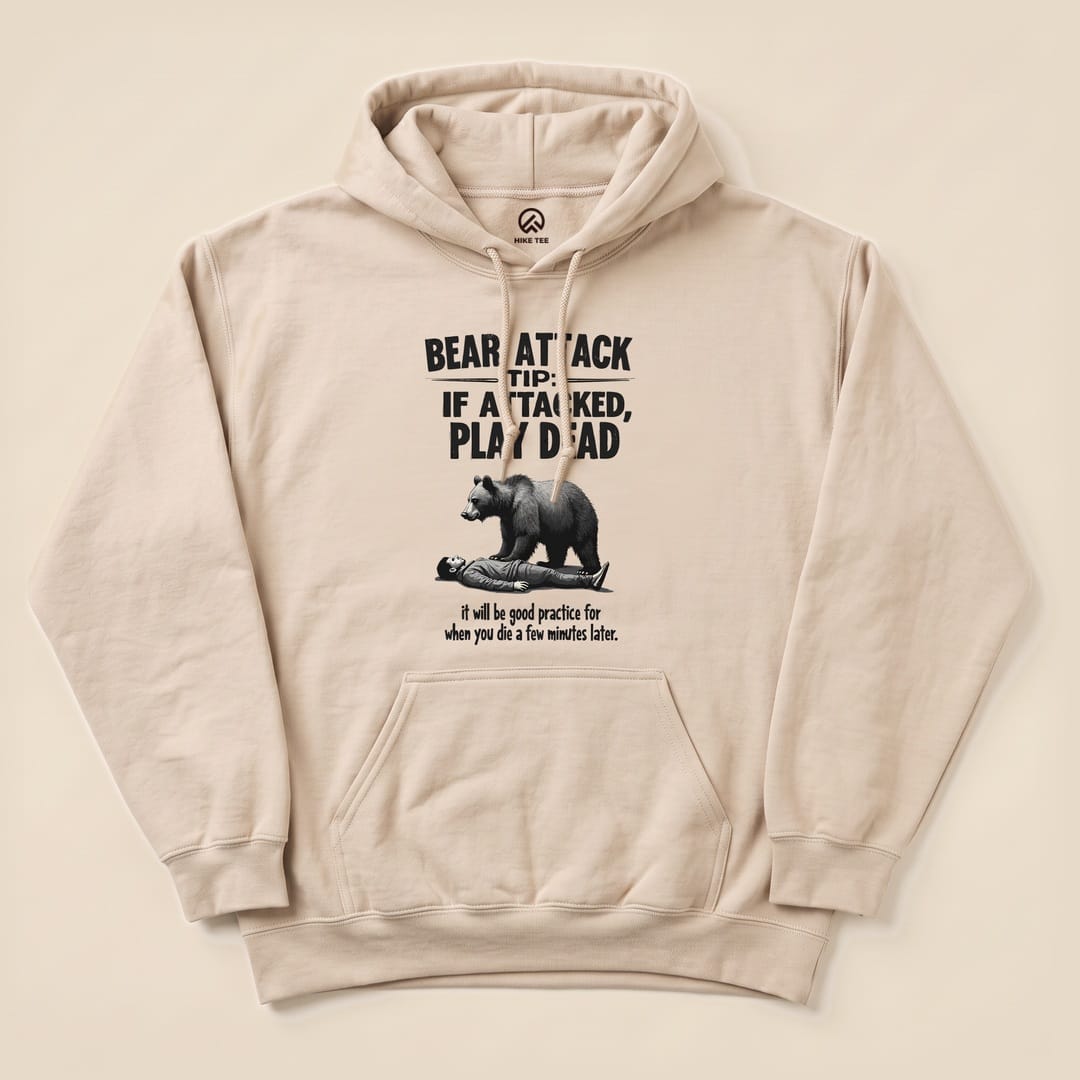 A graphic t-shirt featuring the slogan "Bear Attack Tip: If Attacked, Play Dead" with a bear looming over a person, titled "Play Dead Bear Attack Tip Hoodie.