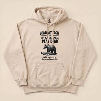 A graphic t-shirt featuring the slogan "Bear Attack Tip: If Attacked, Play Dead" with a bear looming over a person, titled "Play Dead Bear Attack Tip Hoodie.