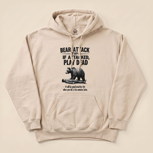 A graphic t-shirt featuring the slogan "Bear Attack Tip: If Attacked, Play Dead" with a bear looming over a person, titled "Play Dead Bear Attack Tip Hoodie.