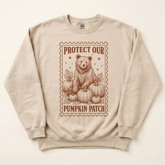 A beige sweatshirt featuring a graphic of a bear surrounded by pumpkins and the slogan "Protect Our Pumpkin Patch.