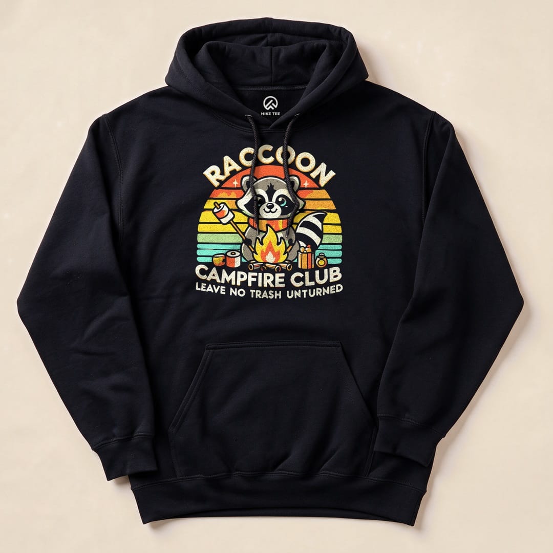 A black hoodie featuring a colorful "Raccoon Campfire Club" graphic with a raccoon by a campfire and the slogan "Leave No Trash Unturned.