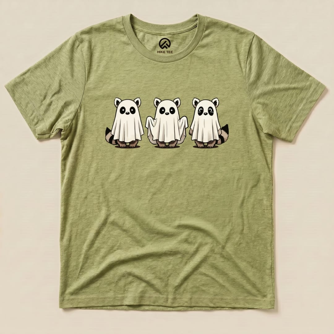 A graphic t-shirt featuring three cartoon raccoons dressed as ghosts on a light green background, labeled as the "Raccoon Ghosts Shirt.