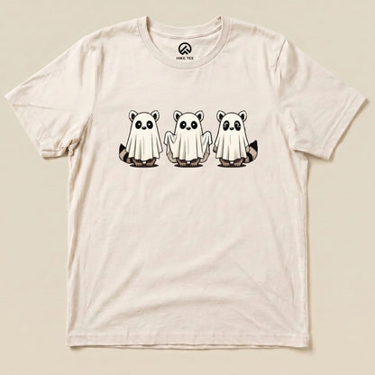 A graphic t-shirt featuring three cute raccoons dressed as ghosts, printed on a light-colored fabric, labeled as the "Raccoon Ghosts Shirt.