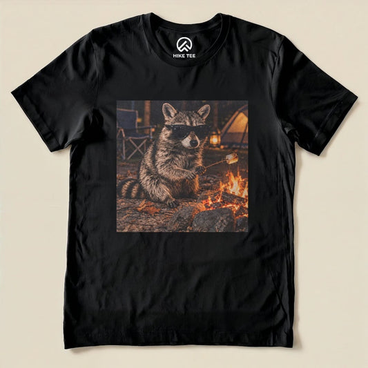 A graphic t-shirt featuring a raccoon in sunglasses sitting by a campfire, ready to roast marshmallows.