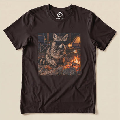 A graphic t-shirt featuring a raccoon wearing sunglasses while roasting marshmallows over a campfire, titled "Raccoon in Sunglasses Shirt.