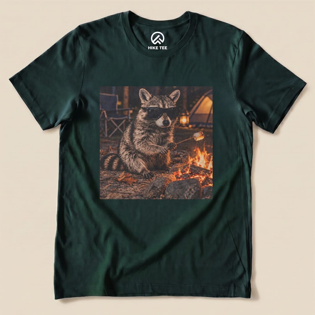 A graphic t-shirt featuring a raccoon in sunglasses sitting by a campfire, holding a marshmallow on a stick.