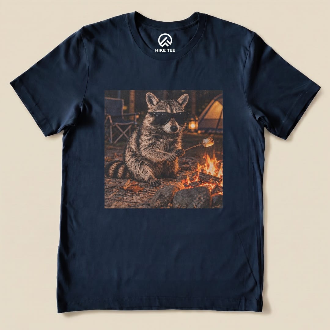 A graphic t-shirt featuring a raccoon in sunglasses sitting by a campfire, holding a marshmallow on a stick.