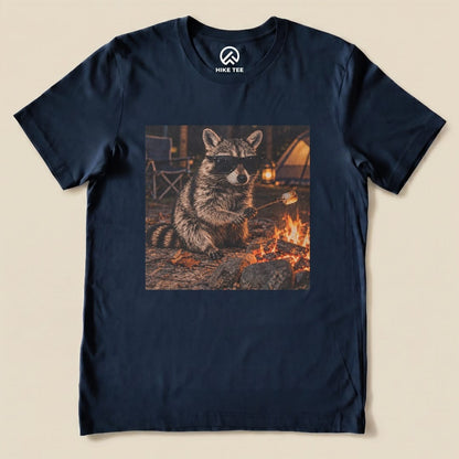 A graphic t-shirt featuring a raccoon in sunglasses sitting by a campfire, holding a marshmallow on a stick.