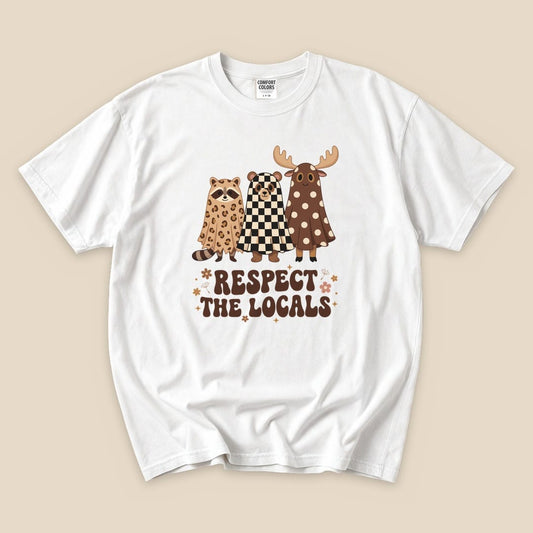 A white graphic t-shirt featuring a raccoon, bear, and moose dressed as ghosts with the text "RESPECT THE LOCALS.