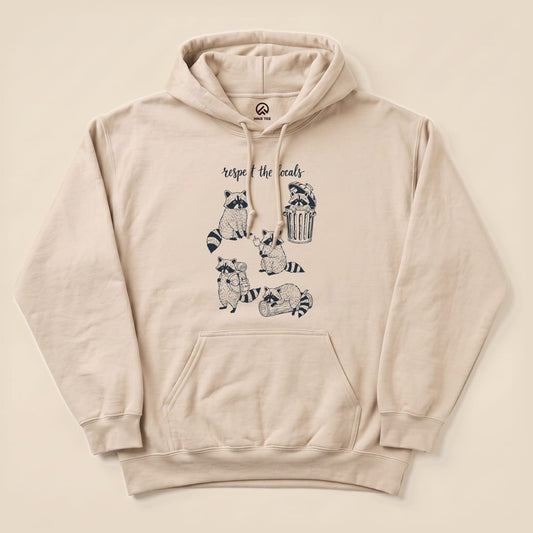 The “Respect the Raccoons Hoodie” features a playful graphic of raccoons engaging in quirky activities, printed on a beige hoodie.