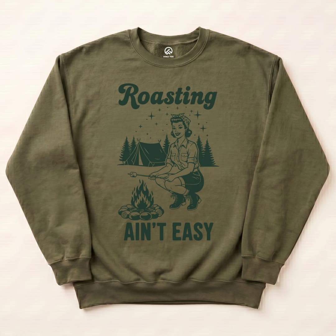 The Roasting Retro Sweatshirt features a playful graphic of a woman roasting marshmallows by a campfire, surrounded by trees and a tent.