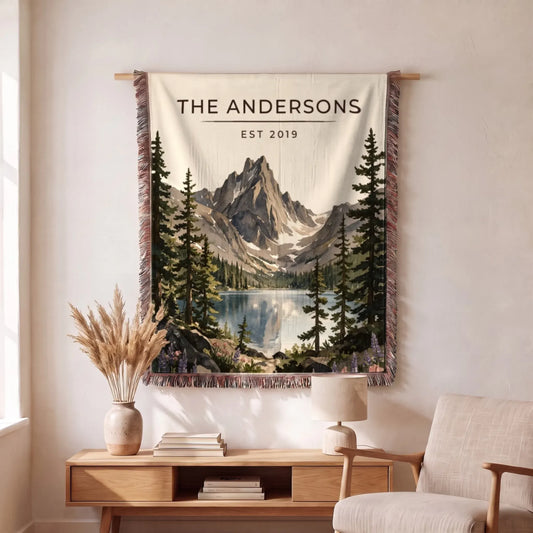 A beautiful Rocky Mountain Dream Lake Woven Blanket hangs on a wall, featuring a scenic mountain and lake landscape.