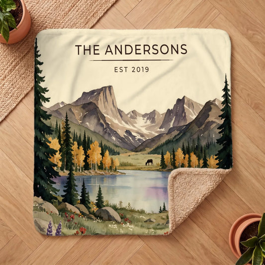 A beautifully illustrated Rocky Mountain Lake Elk Sherpa Blanket featuring a serene landscape of mountains and a lake.