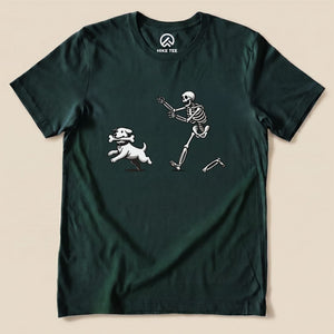A dark green graphic t-shirt features a playful skeleton chasing a white dog with a bone, highlighting the Skeleton and Dog Shirt design.