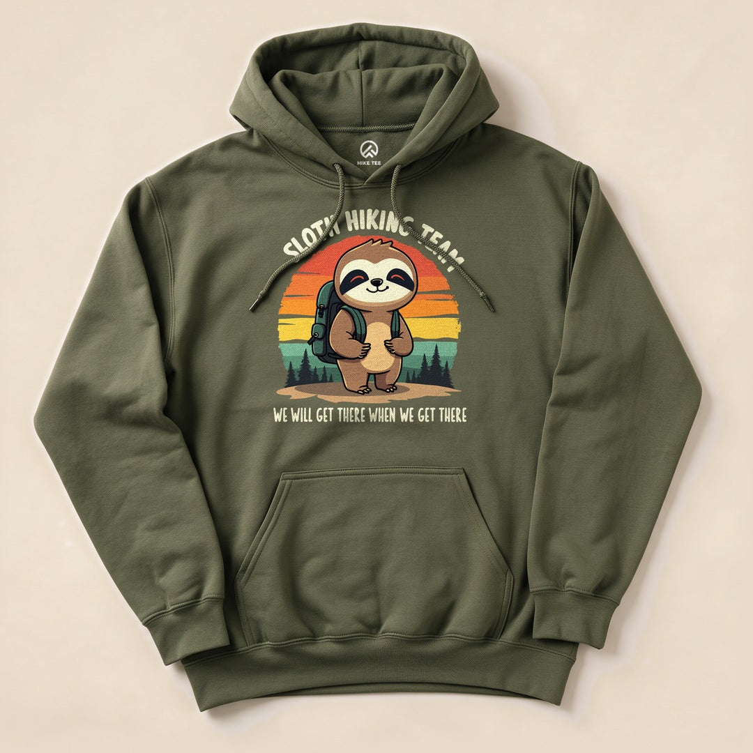 Olive green hoodie featuring a sloth with a backpack, surrounded by trees and a sunset, labeled "Sloth Hiking Team Forest Hoodie".