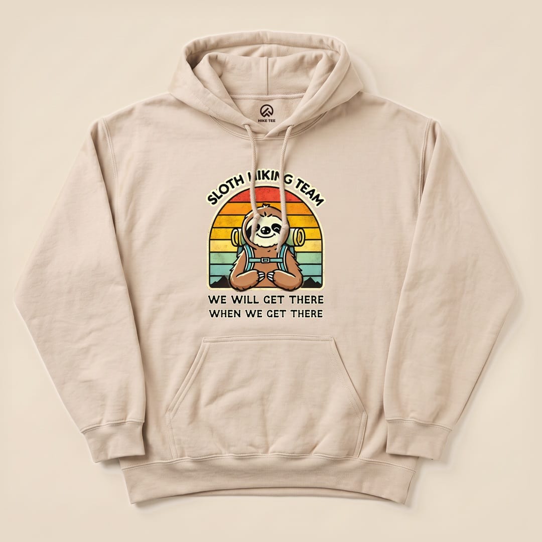 A beige hoodie featuring a graphic of a smiling sloth with the text "Sloth Hiking Team" and "We Will Get There When We Get There.