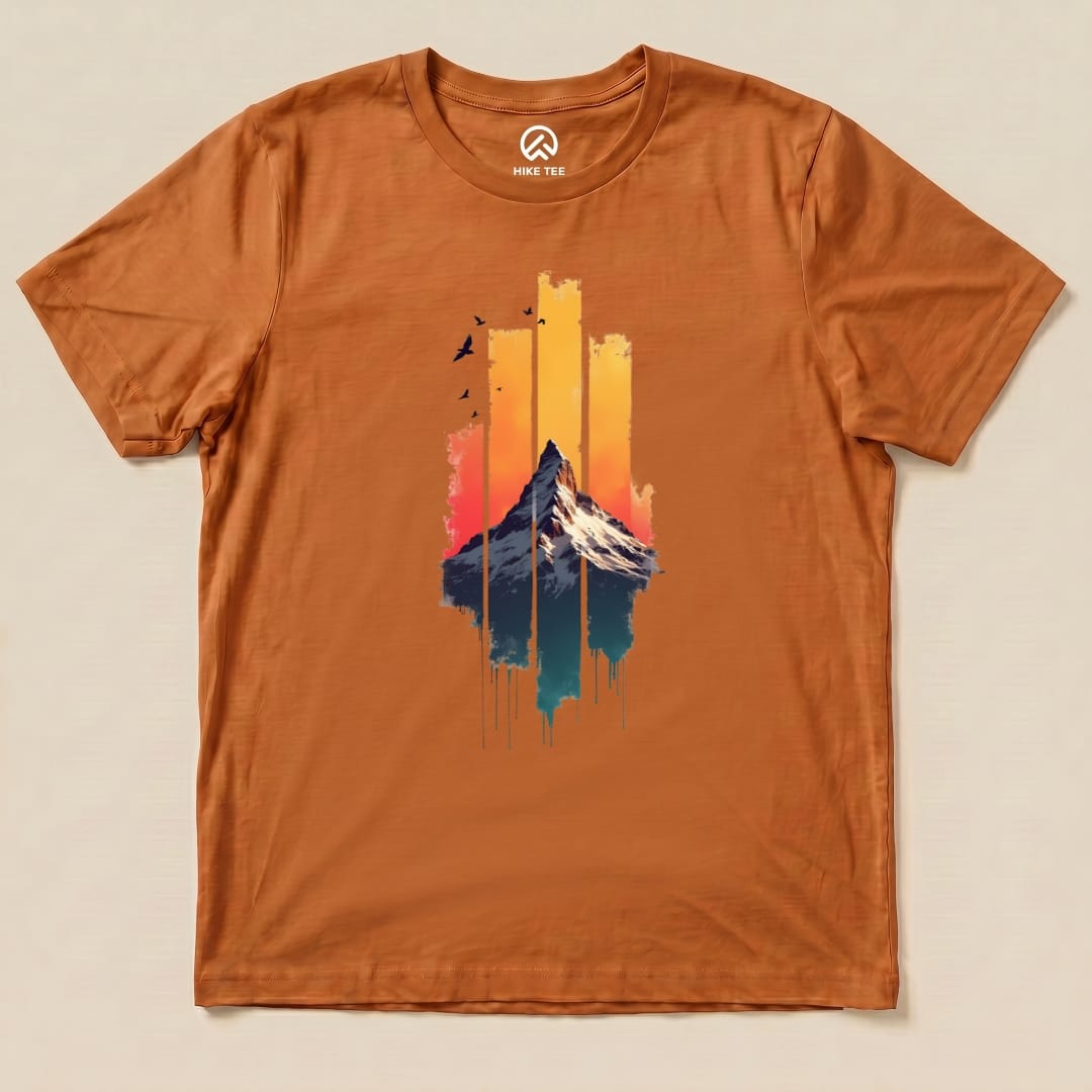A flat view of a graphic t-shirt in orange featuring a colorful mountain illustration and the phrase "Snow Mountain Sunset Shirt.