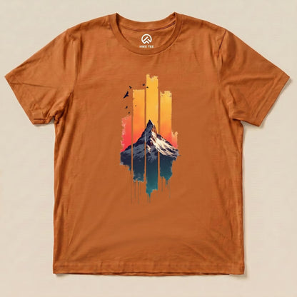 A flat view of a graphic t-shirt in orange featuring a colorful mountain illustration and the phrase "Snow Mountain Sunset Shirt.