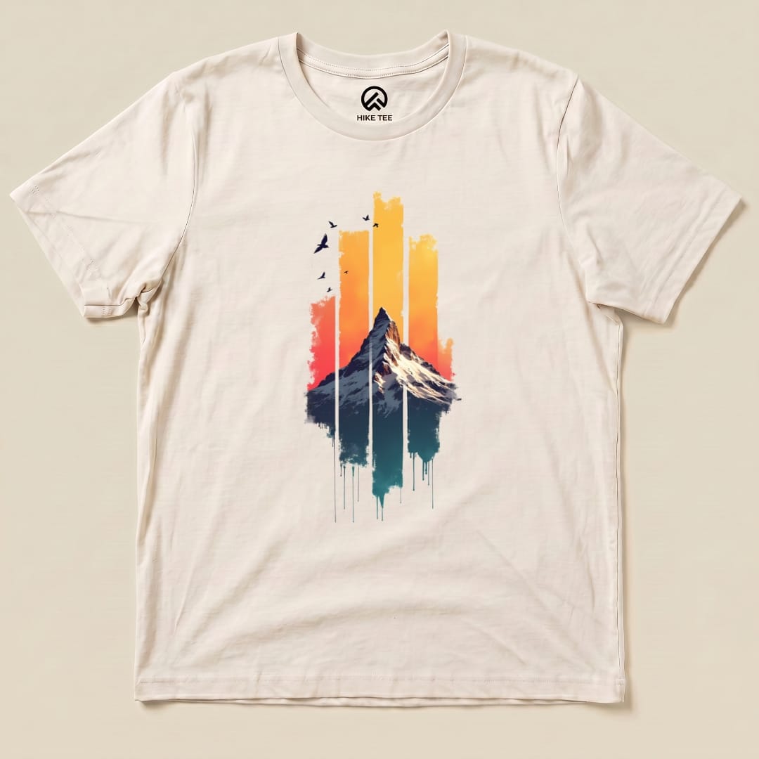 The Snow Mountain Sunset Shirt features a graphic of a mountain against a sunset backdrop with streaks of color and birds above.