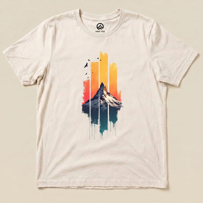 The Snow Mountain Sunset Shirt features a graphic of a mountain against a sunset backdrop with streaks of color and birds above.