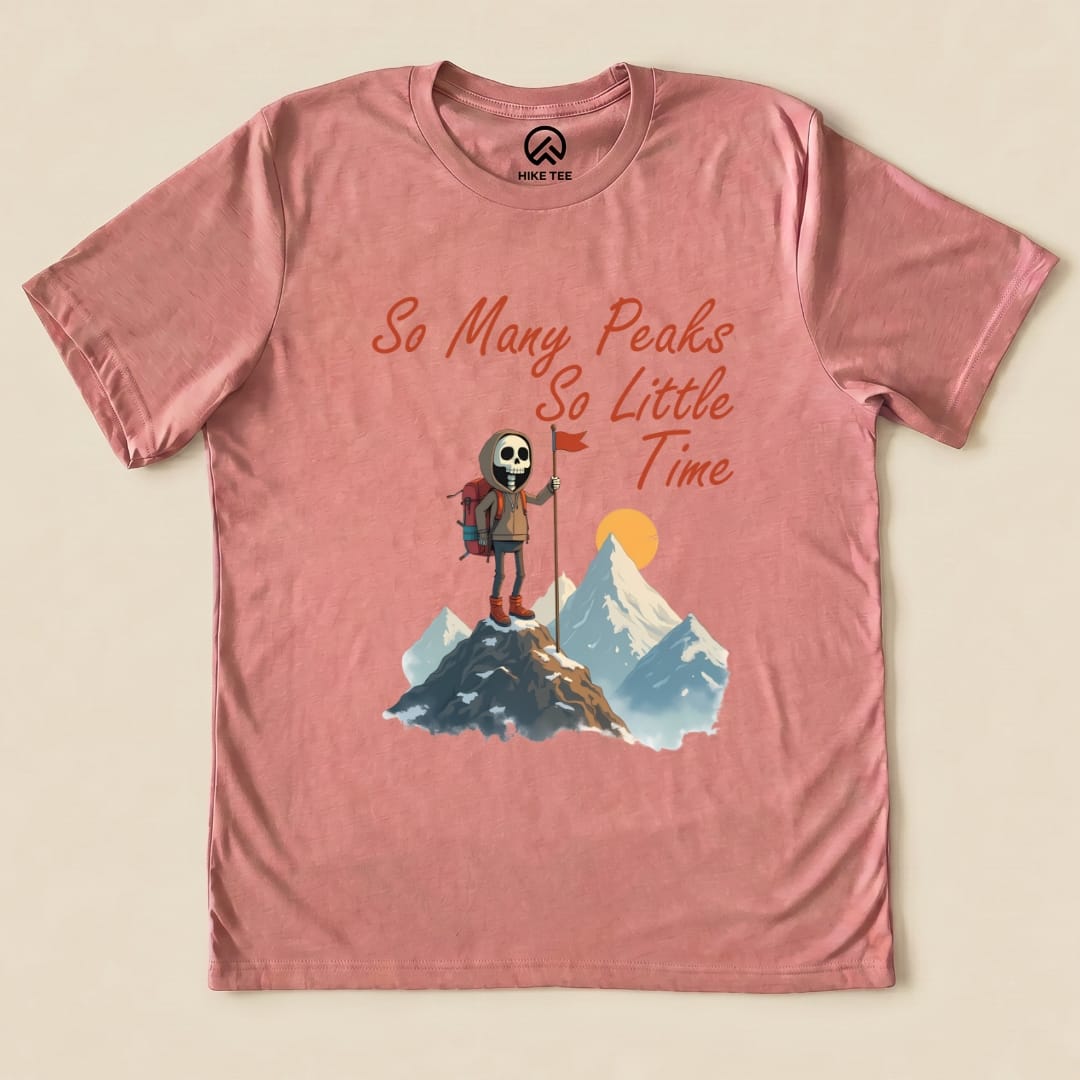 The graphic t-shirt features a playful design with a skeleton hiker holding a flag, captioned "So Many Peaks So Little Time".