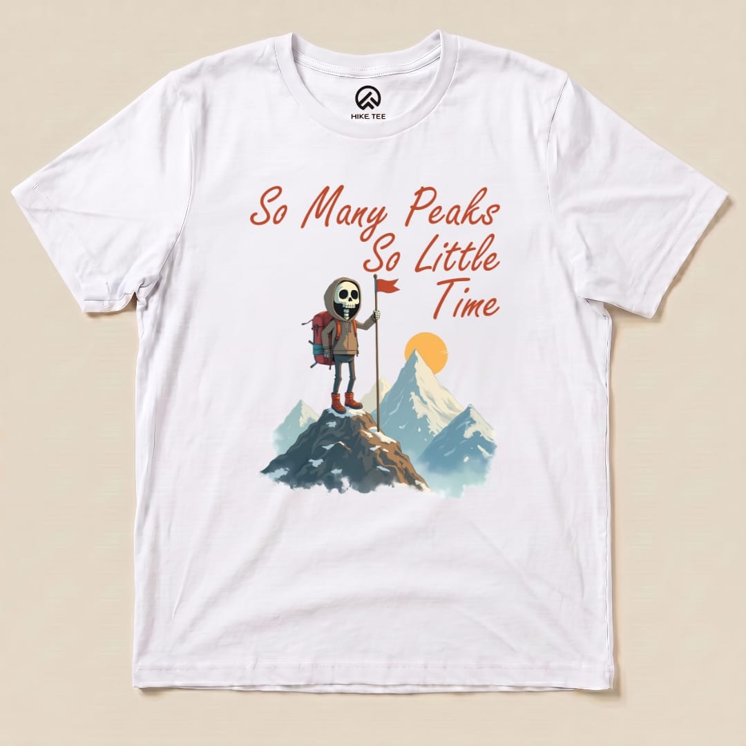 A graphic t-shirt displays the "So Many Peaks Shirt" with a skeleton hiker on a mountain, holding a red flag and surrounded by peaks.