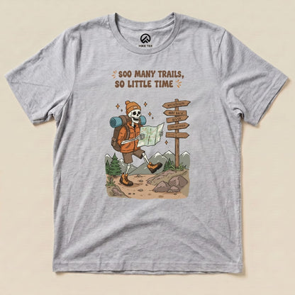 A graphic t-shirt featuring a skeleton hiker with a map, surrounded by trails and signs, captioned "So Many Trails, So Little Time.