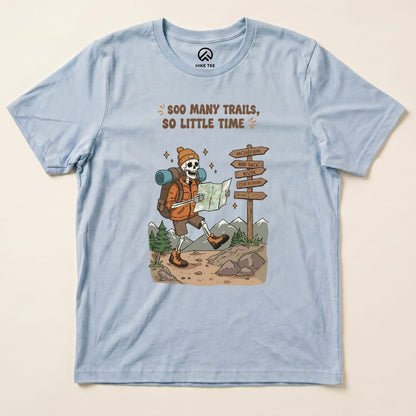 Graphic t-shirt featuring a cartoon skeleton hiking with a map and the slogan "So Many Trails, So Little Time" printed above.