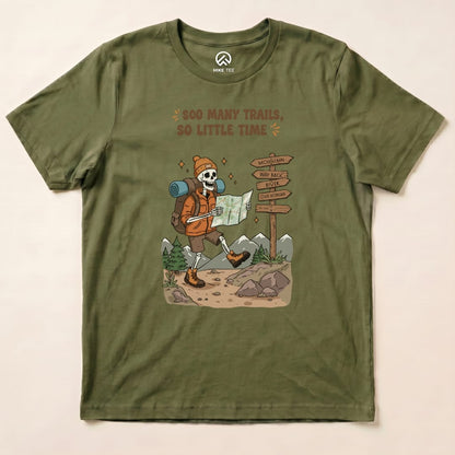 A graphic t-shirt in olive green featuring a skeleton backpacker with the slogan "So Many Trails, So Little Time" next to a trail sign.
