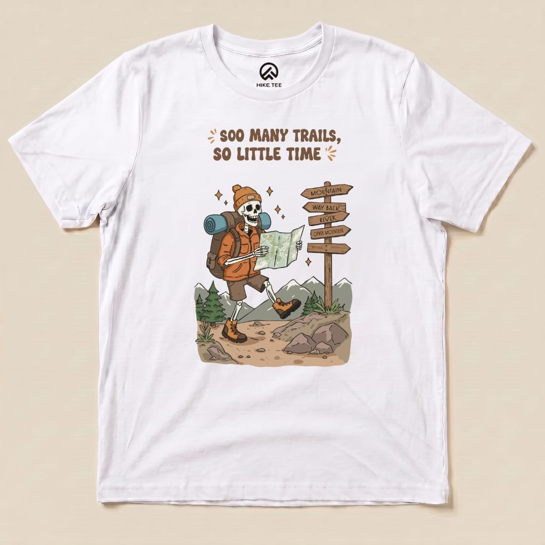 A graphic t-shirt featuring a skeleton in hiking gear reading a map, showcasing the phrase "So Many Trails, So Little Time.