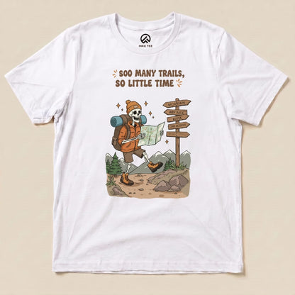 A graphic t-shirt featuring a skeleton in hiking gear reading a map, showcasing the phrase "So Many Trails, So Little Time.