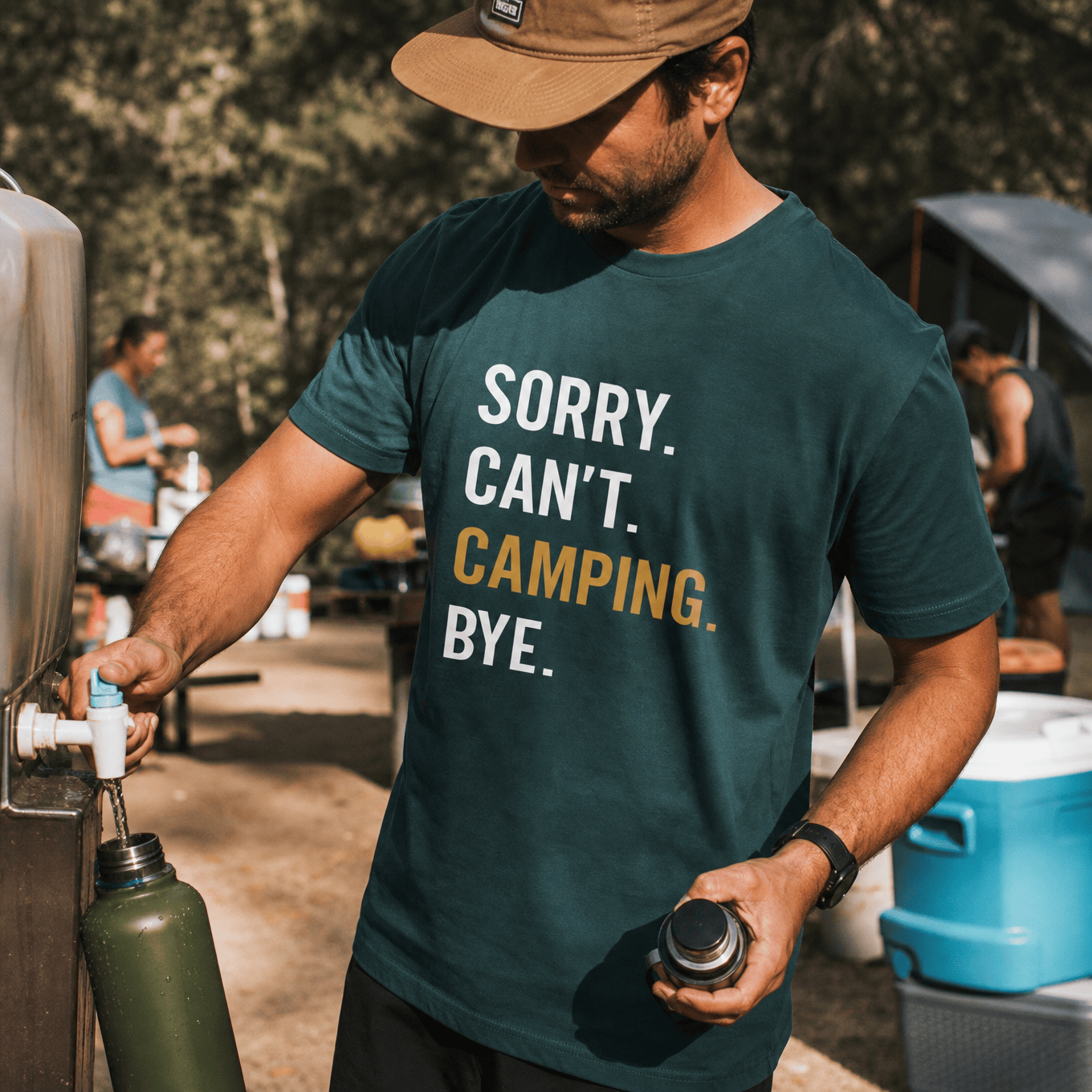 A man at a campsite is filling a water bottle while wearing a dark green graphic t-shirt that says, "Sorry. Can't. Camping. Bye.