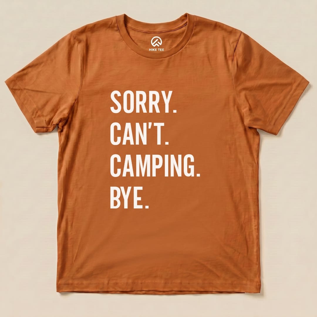 A flat, orange graphic t-shirt featuring the bold text "Sorry. Can't. Camping. Bye." displayed prominently on the front.
