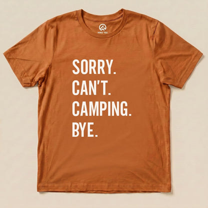 A flat, orange graphic t-shirt featuring the bold text "Sorry. Can't. Camping. Bye." displayed prominently on the front.
