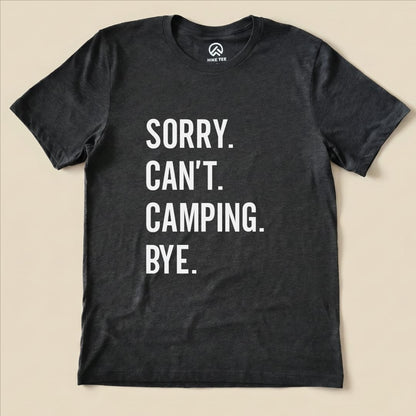 A flat lay of a dark graphic t-shirt displaying the text "Sorry. Can't. Camping. Bye." in bold white letters.