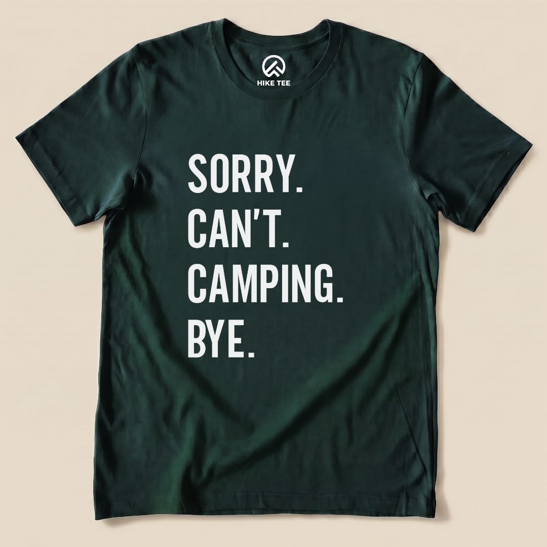 A flat lay image of a dark green graphic t-shirt featuring the text "Sorry. Can't. Camping. Bye." in bold white letters.