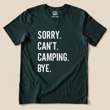 A flat lay image of a dark green graphic t-shirt featuring the text "Sorry. Can't. Camping. Bye." in bold white letters.