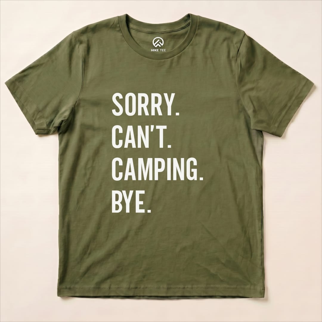 A flat olive green graphic t-shirt featuring the text "Sorry. Can't. Camping. Bye." in bold white letters.