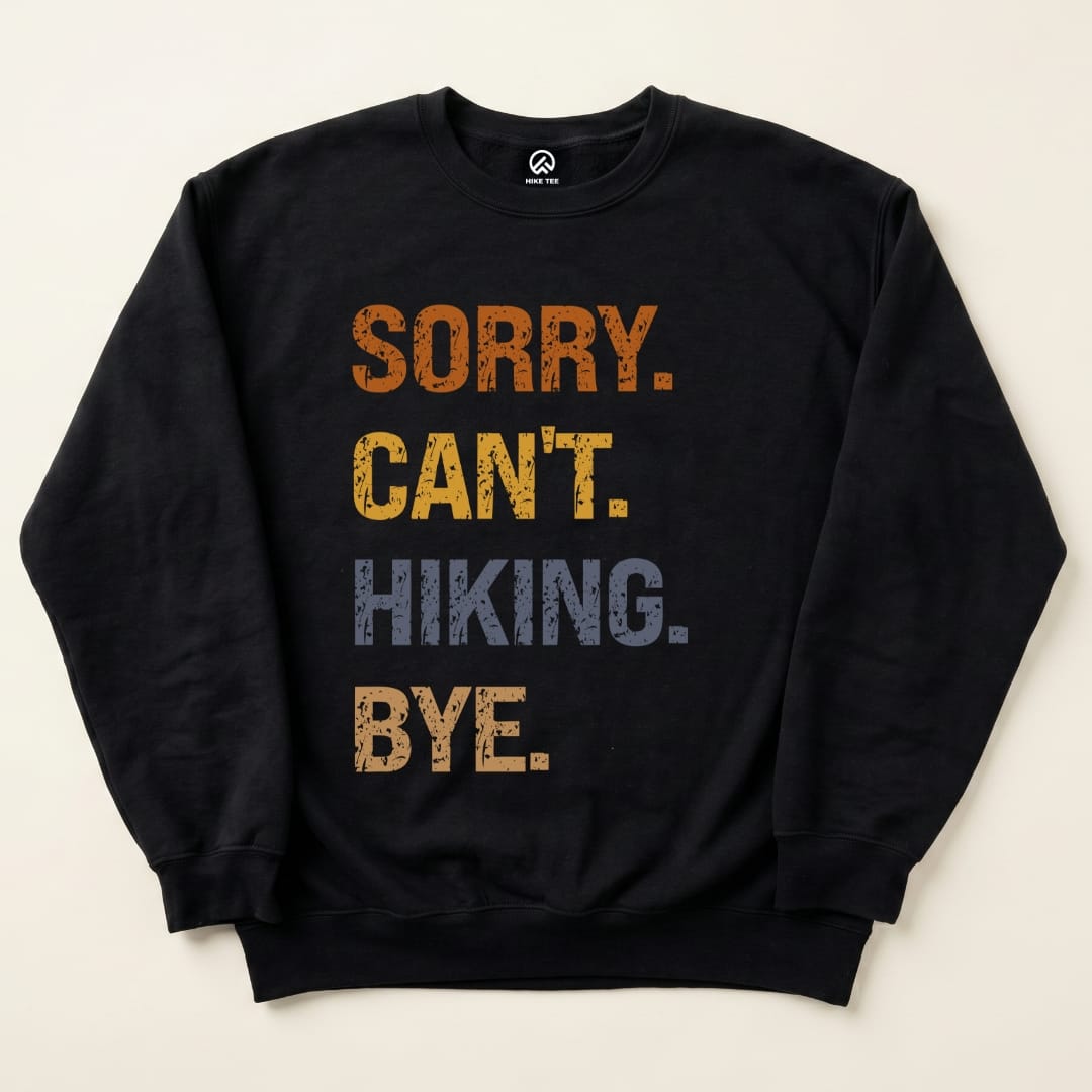 A flat lay of the "Sorry Can't Hiking Bye Sweatshirt" features bold text in orange, yellow, and blue on a black background.