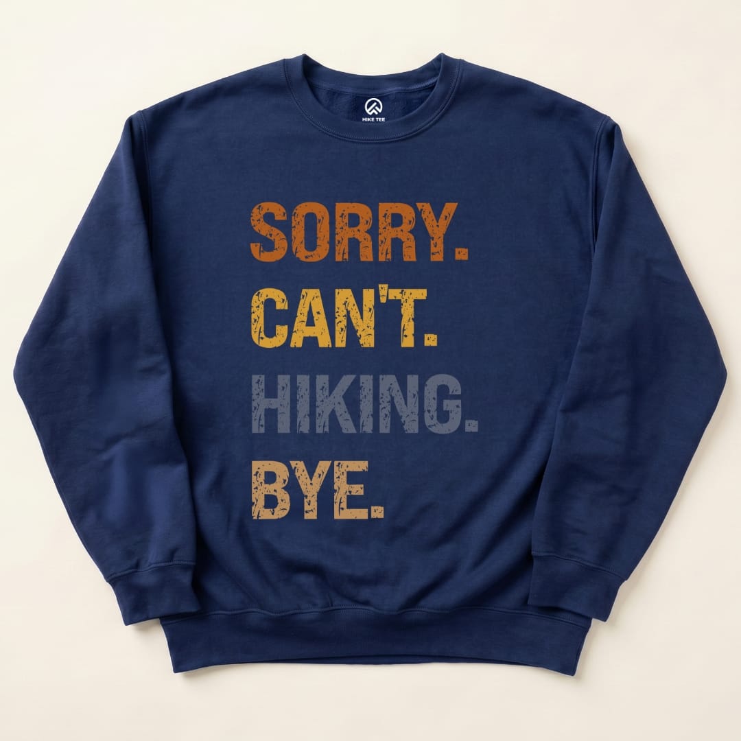 A navy sweatshirt features the humorous slogan "Sorry Can't. HIKING. Bye." in bold, distressed fonts, showcasing its graphic design.