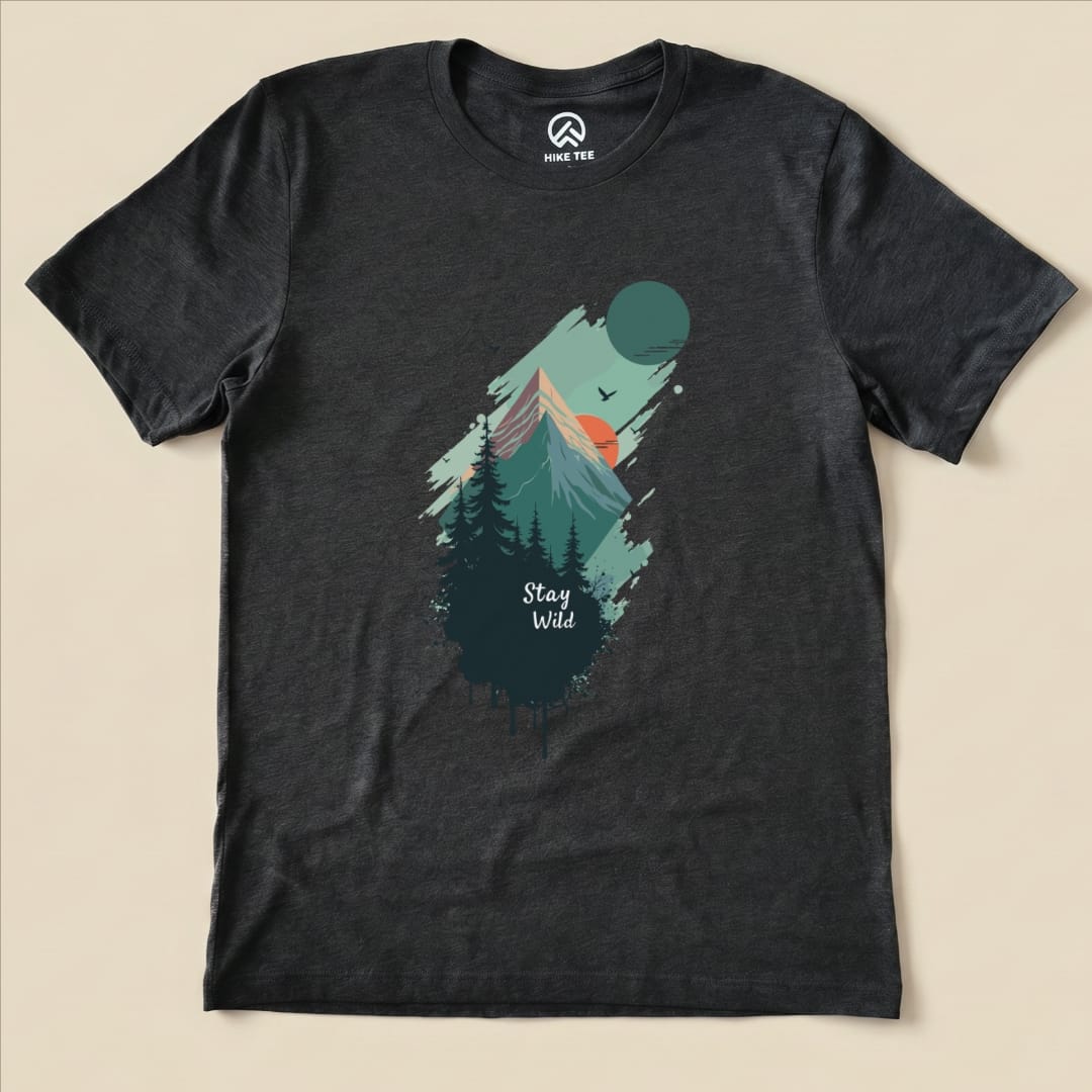 The Stay Wild Shirt features a graphic design of mountains, trees, and a sunset with the slogan "Stay Wild" prominently displayed.