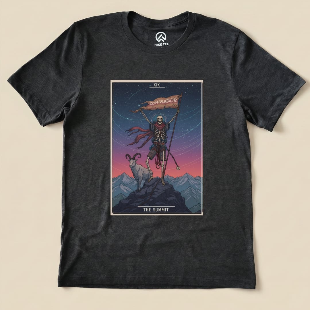 A black graphic t-shirt featuring a skeleton holding a flag labeled "CONQUEROR," accompanied by a goat against a mountain backdrop, titled "The Summit Tarrot Card Shirt.