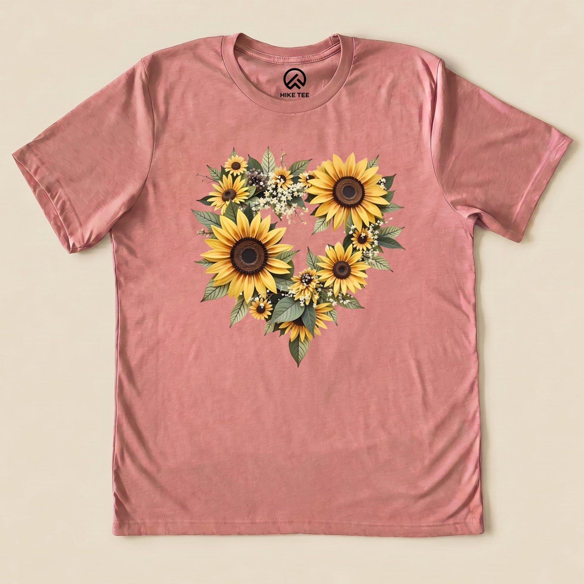 A graphic t-shirt in pink featuring a heart shape made of vibrant sunflowers and green leaves, titled "Sunflowers Heart Shirt.