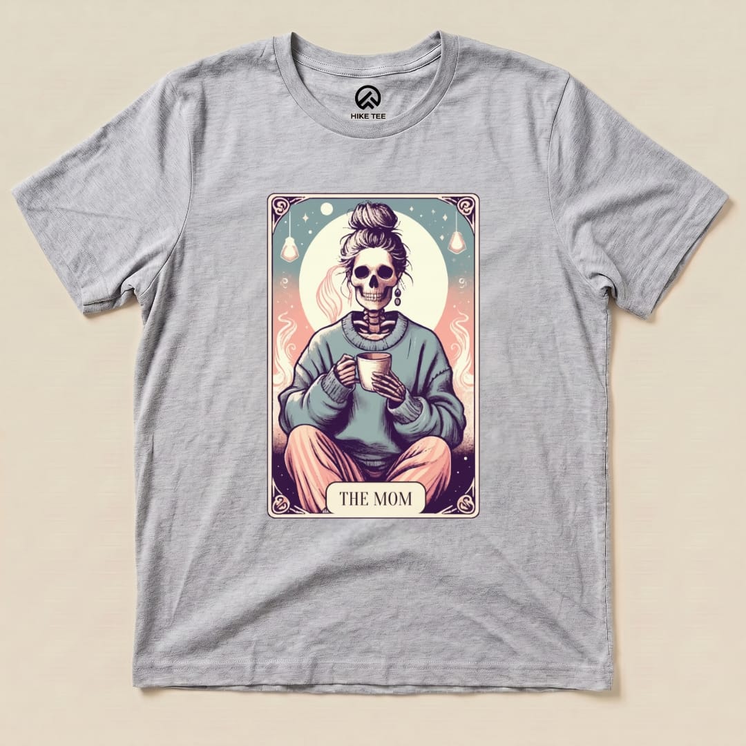 A graphic t-shirt featuring a skeleton mom holding a cup, with the words "THE MOM" in a colorful tarot card design.