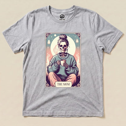 A graphic t-shirt featuring a skeleton mom holding a cup, with the words "THE MOM" in a colorful tarot card design.